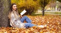 Pretty girl reads book in autumn park. Young woman sits on background of nature Royalty Free Stock Photo