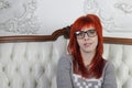 Pretty girl with red hair in glasses sits on white sofa Royalty Free Stock Photo