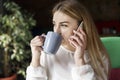 Pretty girl is sitting and drinking coffee. She is looking at window. Girl is holding phone close to ear. She wears business suite Royalty Free Stock Photo