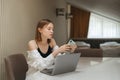 Pretty girl sitting at home in a room at the table and using smartphone and laptop, bright modern interior. Portrait of girl at Royalty Free Stock Photo