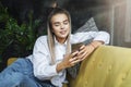 Pretty girl sitting on sofa, playing mobile games on smartphone. Entertainment video content on portable connected