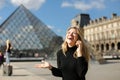 Pretty girl standing near Louvre and glass pyramind in black dress in Paris, talking by smartphone.