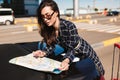 Pretty girl in sunglasses leaning on car dreamily looking road on map with airport on background Royalty Free Stock Photo