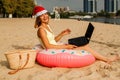 Pretty girl in a swimsuit and santa claus hats using laptop on the beach. Royalty Free Stock Photo