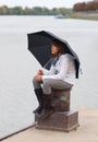 Pretty girl with umbrella sitting on the dock Royalty Free Stock Photo