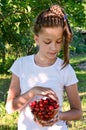 pretty girl in white T-shirt is standing in garden and holding glass vase with red ripe cherries. Concept of gardening Royalty Free Stock Photo