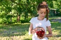 pretty girl in white T-shirt is standing in garden and holding glass vase with red ripe cherries. Concept of gardening Royalty Free Stock Photo