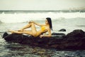 Pretty girl in yellow swimsuit sitting on rocks on beach Royalty Free Stock Photo