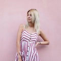 Pretty glamorous young woman with a cute smile with blond hair in a fashionable striped pink dress posing standing Royalty Free Stock Photo