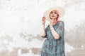 Pretty gorgeous young woman with chic pink hair in fashionable white  hat in summer stylish blue floral dress posing near wall on Royalty Free Stock Photo