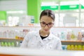 A pretty graceful dark-haired lady with glasses, dressed in a white coat, carefully examies the goods on the shelf in