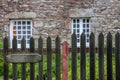 A pretty stone cottage with stone lintels and white mullioned windows stands surrounded by grass and a picket fence. Royalty Free Stock Photo