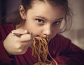 Pretty grimacing kid girl eating tasty spaghetti on the dinner on the home kitchen. Closeup