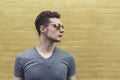 Pretty handsome confident young man hipster with sunglasses smiling behind yellow wall. Looking aside. Horizontal.