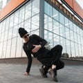 Pretty handsome young hipster man dancer in knitted hat in stylish black clothes in trendy sunglasses dancing break dance