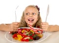 Pretty happy Caucasian female child eating dish full of candy in sweet sugar abuse dangerous diet