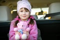 Pretty happy child girl playing with a pink toy teddy bear sitting in a car trunk Royalty Free Stock Photo