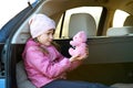 Pretty happy child girl playing with a pink toy teddy bear sitting in a car trunk Royalty Free Stock Photo