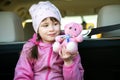 Pretty happy child girl playing with a pink toy teddy bear sitting in a car trunk Royalty Free Stock Photo