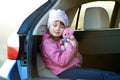 Pretty happy child girl playing with a pink toy teddy bear sitting in a car trunk Royalty Free Stock Photo