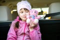 Pretty happy child girl playing with a pink toy teddy bear sitting in a car trunk Royalty Free Stock Photo