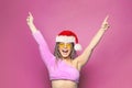 Pretty happy excited Christmas woman Santa posing against bright pink studio wall background. Xmas offer, gift and New Year partry