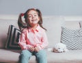 Pretty happy little girl in casual wearing sitting on sofa with toy dog and smiling. Royalty Free Stock Photo