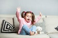 Pretty happy little girl in casual wearing sitting on sofa with toy dog and smiling. Royalty Free Stock Photo