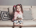 Pretty happy little girl in casual wearing sitting on sofa with toy dog and smiling. Royalty Free Stock Photo