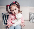 Pretty happy little girl in casual wearing sitting on sofa with toy dog and smiling. Royalty Free Stock Photo