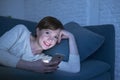 Pretty and happy red hair woman on her 20s or 30s lying on home couch or bed using mobile phone late at night smiling in internet Royalty Free Stock Photo