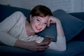 Pretty and happy red hair woman on her 20s or 30s lying on home couch or bed using mobile phone late at night smiling in internet Royalty Free Stock Photo