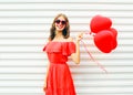 Pretty happy smiling woman in red dress and sunglasses with air balloons heart shape walking at city over white Royalty Free Stock Photo