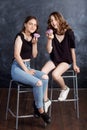 Pretty happy teenage girls with donuts  siting on chairs and having fun. Portrait of joyful smiling girls with donuts on black Royalty Free Stock Photo