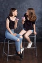 Pretty happy teenage girls with donuts  siting on chairs and having fun. Portrait of joyful smiling girls with donuts on black Royalty Free Stock Photo