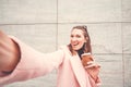 Pretty and happy urban woman taking selfie on a marble background. She holds a coffee cup in left hand and smartphone to take phot