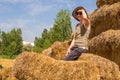 Pretty happy woman with hat leaning against the straw bales and looking away on a sunny day. Royalty Free Stock Photo