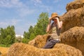 Pretty happy woman with hat sitting on straw bales covering her eyes with her hands. Royalty Free Stock Photo