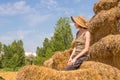 Pretty happy woman with hat sitting on straw bales and getting some rest. Royalty Free Stock Photo