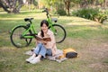 A pretty and happy young Asian woman is relaxing and reading a book in a green park on a bright day Royalty Free Stock Photo