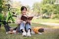 A pretty and happy young Asian woman is relaxing and reading a book in a green park on a bright day Royalty Free Stock Photo