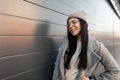 Pretty happy young hipster woman with cute smile in glasses in sweater in knitted fashionable hat in gray trendy coat in the city Royalty Free Stock Photo