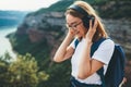 Pretty happy young tourist woman with backpack and  hipster glasses smiling listens favorite music with headphones enjoying Royalty Free Stock Photo