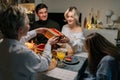 Pretty happy young woman receiving gift from loving mother-in-law sitting with family at dinner feast table at home on Royalty Free Stock Photo