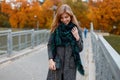 Pretty happy young woman in a vintage autumn stylish coat in a fashionable green scarf with a leather handbag is standing