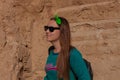 Pretty hiker girl with traveling backpack moving up on the mountain road. Smiling traveler woman looking away