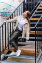 Pretty hipster girl is standing on stairs, Happy beautiful young woman in leather green pants and light beige jacket, urban Royalty Free Stock Photo