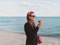 Pretty hipster woman in bandana long hair walking on sea background with coffee cup lifestyle real life travel photo