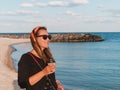 Pretty hipster woman in bandana long hair walking on sea background with coffee cup lifestyle real life travel photo