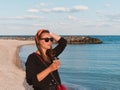 Pretty hipster woman in bandana long hair walking on sea background with coffee cup lifestyle real life travel photo